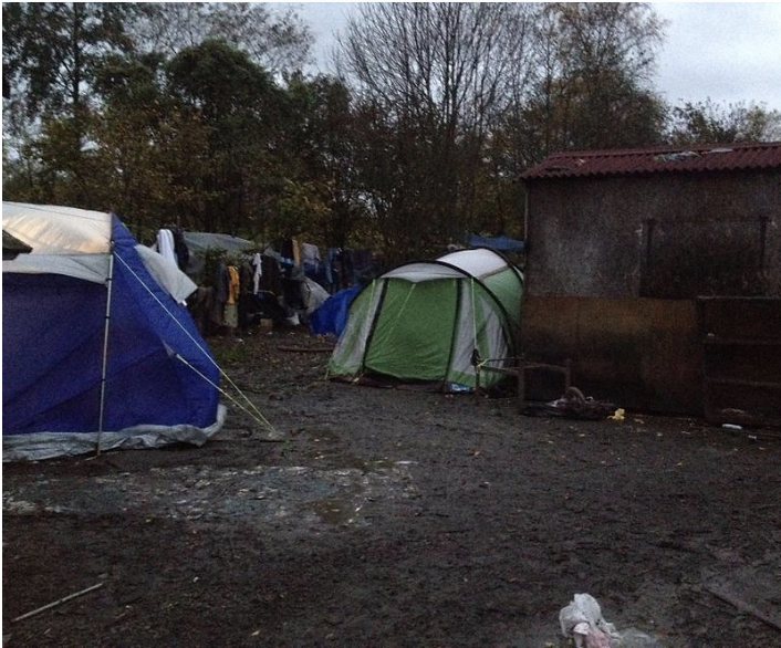 Multiple tents pitched outdoors on muddy ground in cloudy weather.